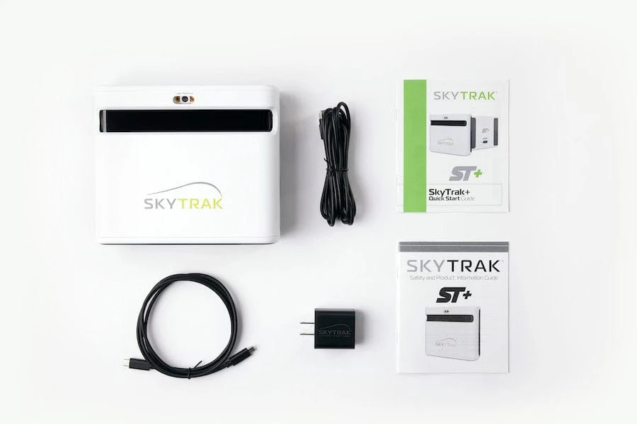 Official SkyTrak ST Plus in-box spread with launch monitor, quick-start guide, safety information, cables, and power block