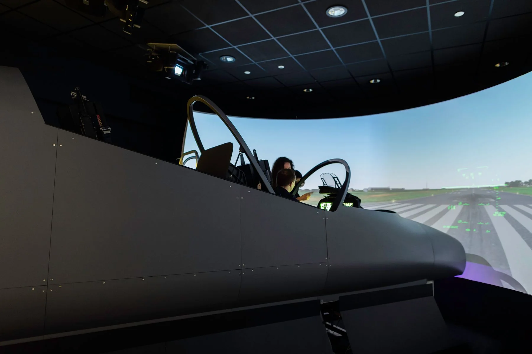 Two people using a professional aircraft flight simulator with a panoramic runway display