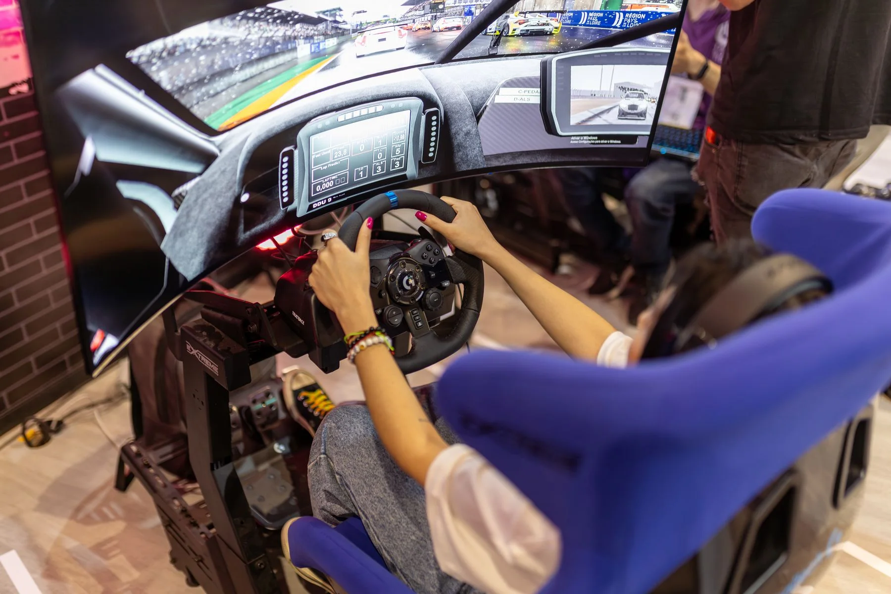 Driver using a full sim racing cockpit with a direct-drive wheel and wraparound display at a gaming event