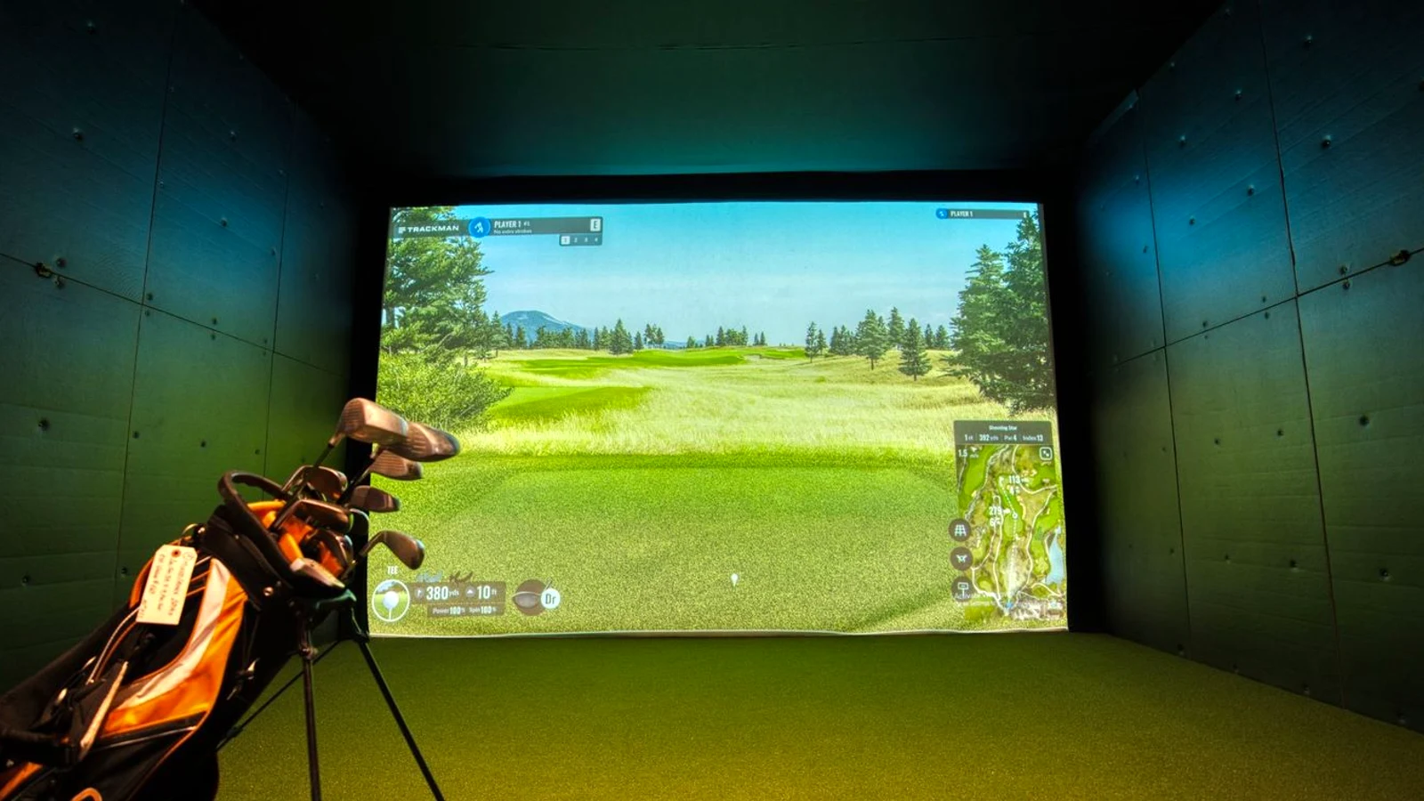 Real indoor golf simulator room in use showing the screen, hitting mat and player scale